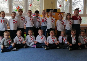 Dzieci z grupy Biedronki ubrane w białe bluzeczki i granatowe spodnie i spódniczki pozują do wspólnego zdjęcia